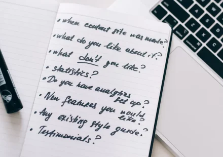 Handwritten checklist in notebook beside a laptop