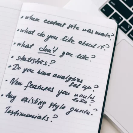 Handwritten checklist in notebook beside a laptop