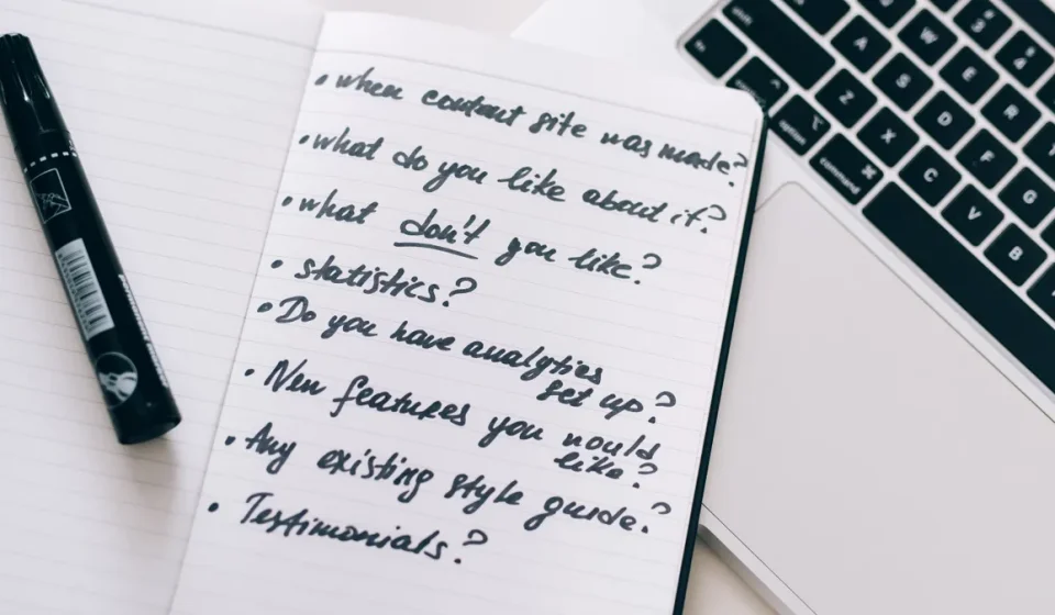 Handwritten checklist in notebook beside a laptop