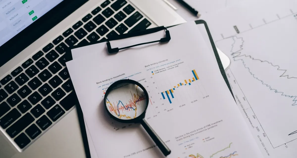 Magnifying glass inspecting printed charts beside a laptop