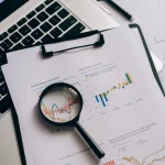 Magnifying glass inspecting printed charts beside a laptop